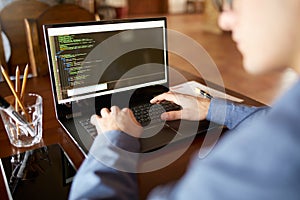 Back view over the shoulder shot of developer programmer with laptop. Program code and script data on the screen. Young