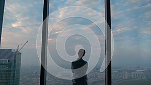 Back view of pensive woman looking at cityscape through window of skyscraper