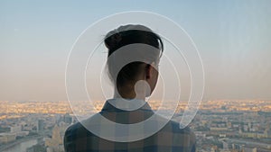 Back view of pensive woman looking at cityscape through window of skyscraper