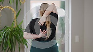 Back view of persistent overweight young woman training reaching hands behind back. Plump Caucasian yogi doing cow face