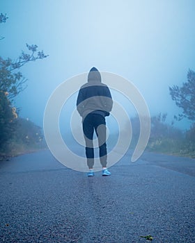 Back view of a person standing on an empty road with fog