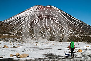 Back view of the person- traveler hiking and tramping with backpack in New Zealand`s mountains, walking toward huge volcano