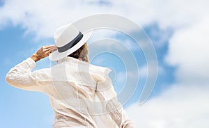 Back view photo of a happy woman looking at the sky. Girl wearing white shirt and summer hat