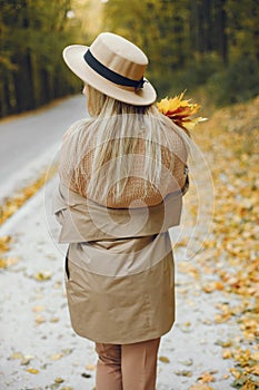 Back view photo of a young blonde girl in a beige hat outdoors on autumn