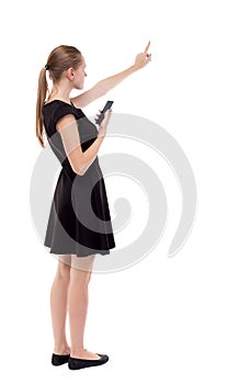 Back view of pointing young beautiful woman and using a mobile phone. The girl in black dress holding shows his