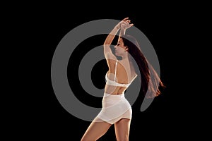 Back view portrait of beautiful sporty young woman in white sportwear posing with arms up against dark mode background.