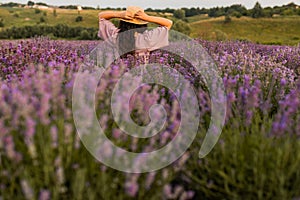 Back view portrait of brunette woman in a straw hat at the lavender field. Stylish female meeting sunset, walking at the