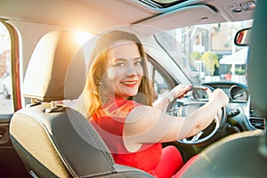 Back view Portrait of business lady, caucasian young woman driver looking at camera and smiling over her shoulder while driving a