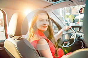 Back view Portrait of business lady, caucasian young woman driver looking at camera and smiling over her shoulder while driving a