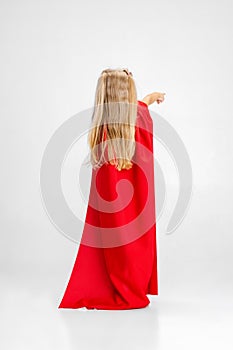 Back view portrait of little Caucasian girl posing like superhero isolated over white studio background.