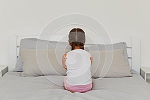 Back view portrait of little girl with dark hair and pigtails, siting backwards to camera, does not want talk with anybody, being