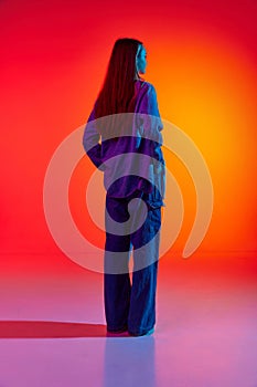 Back view portrait with sad, upset woman, girl with long hair posing over red background in neon light. Spoiled mood