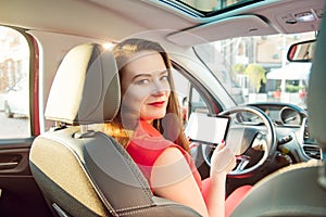 Back view Portrait of smiling caucasian young woman driver looking at camera and holding modern white digital tablet computer pc