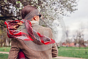 Back view of stylish woman wearing red hair scarf in spring park. Retro female fashion. Headscarf for bun hairstyle