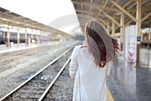 Back view portrait of young asian woman in white dress with sun glassess standing while waiting in train station