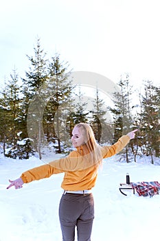 Back view portrait of young woman in winter forest on fir trees background. Walk through the snowy woods. Vertical frame