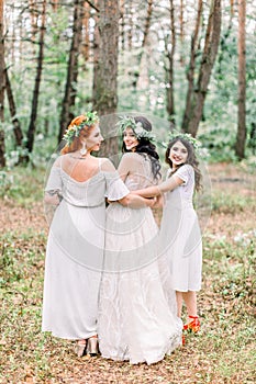 Back view of pretty cheerful bride and bridesmaids in white dresses and floal wreaths having fun at wedding day, walking