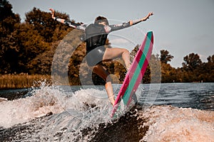 Back view of pretty woman masterfully jumping on wave on surf style wakeboard