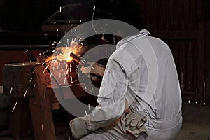 Back view of professional welder man with torch and protective mask welding steel with spark in the factory. Industrial concept.
