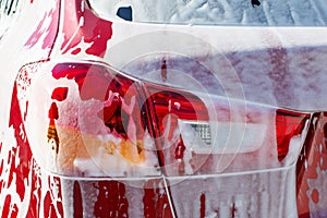 Back view of red compact SUV car with sport and modern design washing with soap. Car covered with white foam.