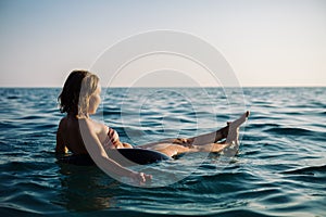 Back view of relaxing woman floating on inflatable ring