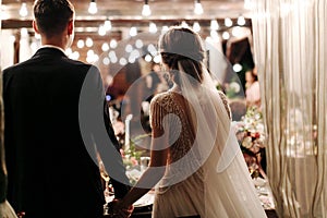 Back view of romantic couple of bride and groom on banquet hand in hand. The lights of the electric garland illuminate the wedding