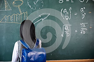 Back view of school girl on science lesson in classroom write an answer on blackboard