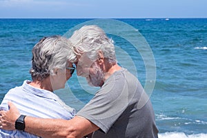 Back view of senior couple in love sitting on the beach looking each other. Two retired enjoying summer vacation and freedom