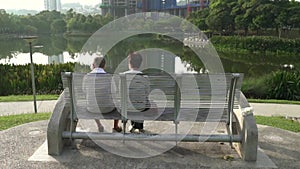 Back view of senior couple sitting on bench in a park.