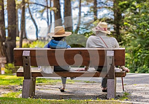 Back view of a senior couple wearing hats sitting on a wooden bench in the park. Reationship. Vancouver Island, BC
