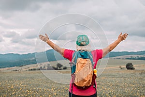 Back view senior happy smiling woman backpacker relaxation on top rocky mountains, with backpack. Leisure after walking