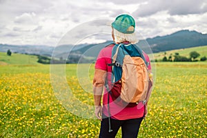 Back view senior happy smiling woman backpacker relaxation on top rocky mountains, with backpack. Leisure after walking