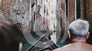 Back view of senior man and woman in gondola excursion tour on very narrow Venice canal in Italy during retirement trip.