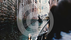 Back view of senior woman enjoying beautiful gondola excursion tour on narrow Venice canal during retirement vacation.