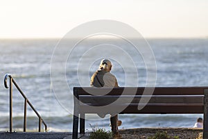 Back view of senior woman sitting on a bench at the beach