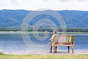 Back view of a senior woman sitting on chair side the lake. Space for text. Concept of aged people and relaxation