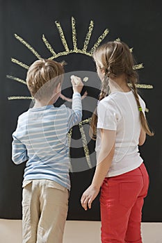 Back view of siblings drawing sun on blackboard