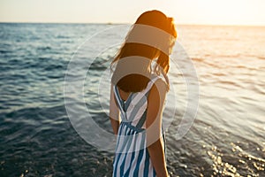 Back view silhouette of portrait brunette beautiful woman walking along beach and sea sunset background. Cover idea. Female in dr