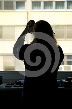 Back view of silhouette of a woman putting on makeup in front of