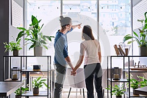 Back view, silhouette of young couple holding hands looking out window