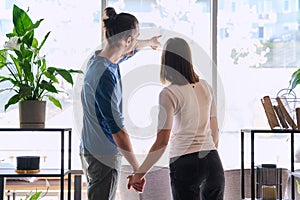 Back view, silhouette of young couple holding hands looking out window