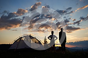 Back view silhouettes of female and kid stand near camping at daybreak