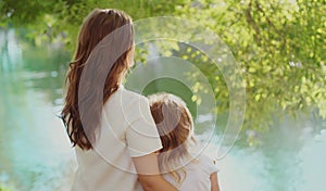 Back view silhouettes of mother and child together on lake in summer