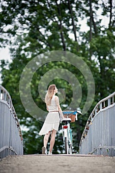 Back view slender female standing with bicycle and enjoing nature on the bridge