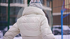 Back view slim woman stretching leg muscles standing with basketball ball at mesh fence on sports ground. Motivated