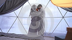Back view slim young woman looking out floor-to-ceiling window in bedroom as man entering hugging smiling. Happy
