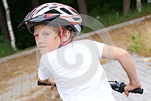 Back view of small boy in protective helmet riding bicycle in park on summer day. Weekend activity.