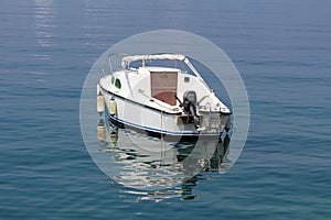 Back view of small white boat with outboard boat motor anchored in local harbor surrounded with calm clear blue sea