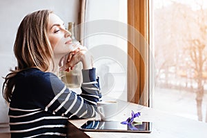 Back view smiling beautiful young woman read magazine with digital tablet near big window in a cafe or home. Attractive