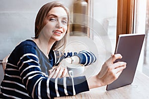 Back view smiling beautiful young woman read magazine with digital tablet near big window in a cafe or home. Attractive